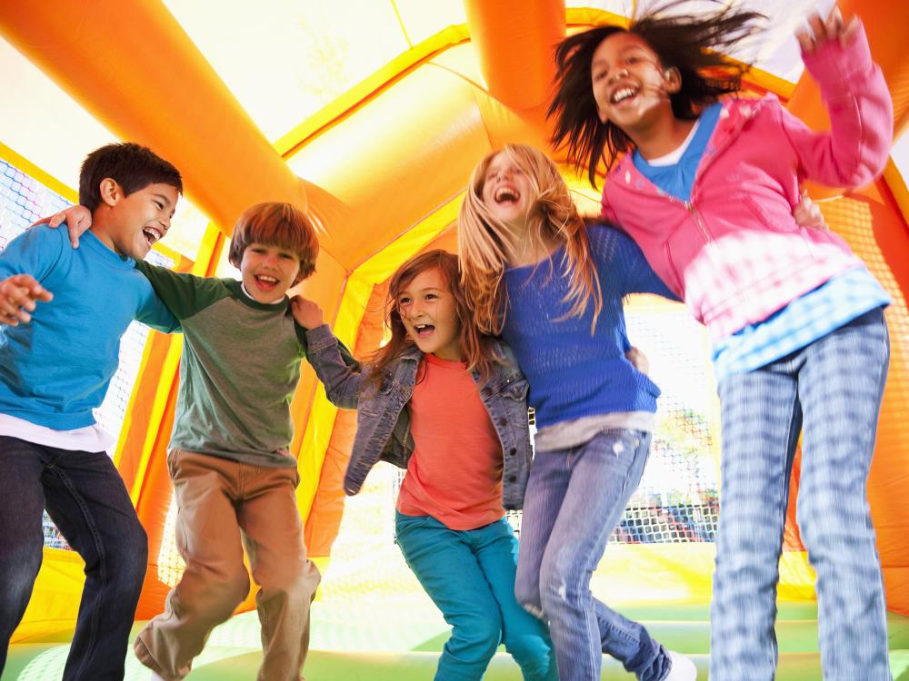 Preteens children of various races, sexes, and ages jumping in a brightly colored bounce house