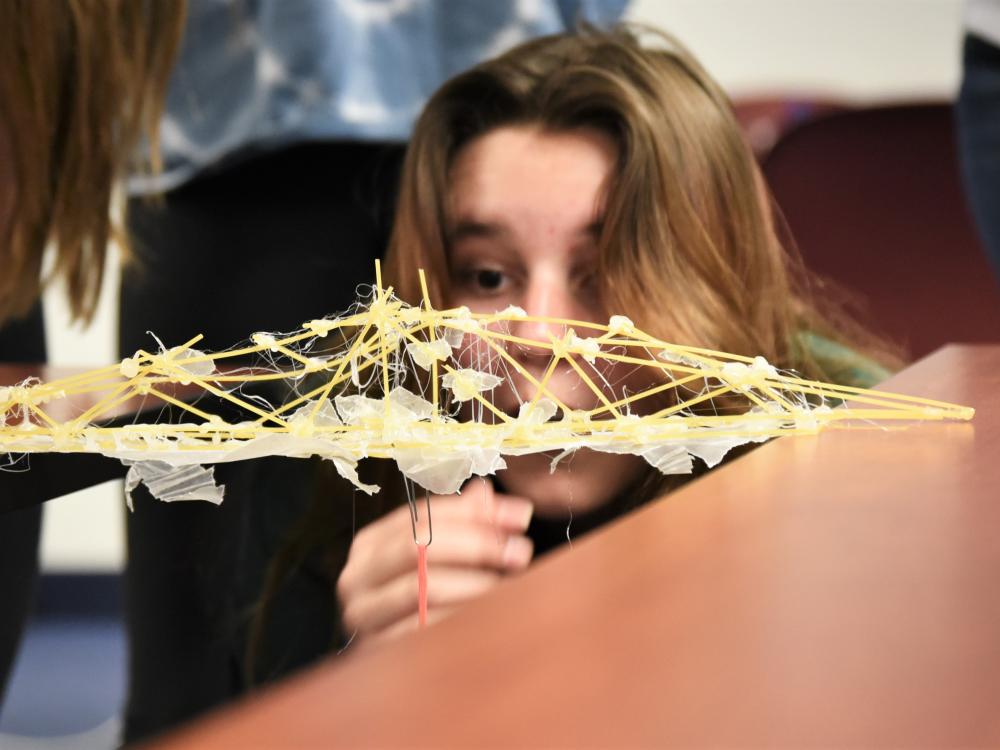 A female student looks closely at a bridge she built with spaghetti noodles.