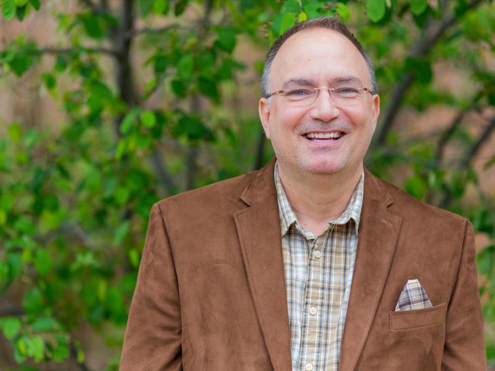 A photo of Dr. John Chapin wearing a brown blazer and standing outside
