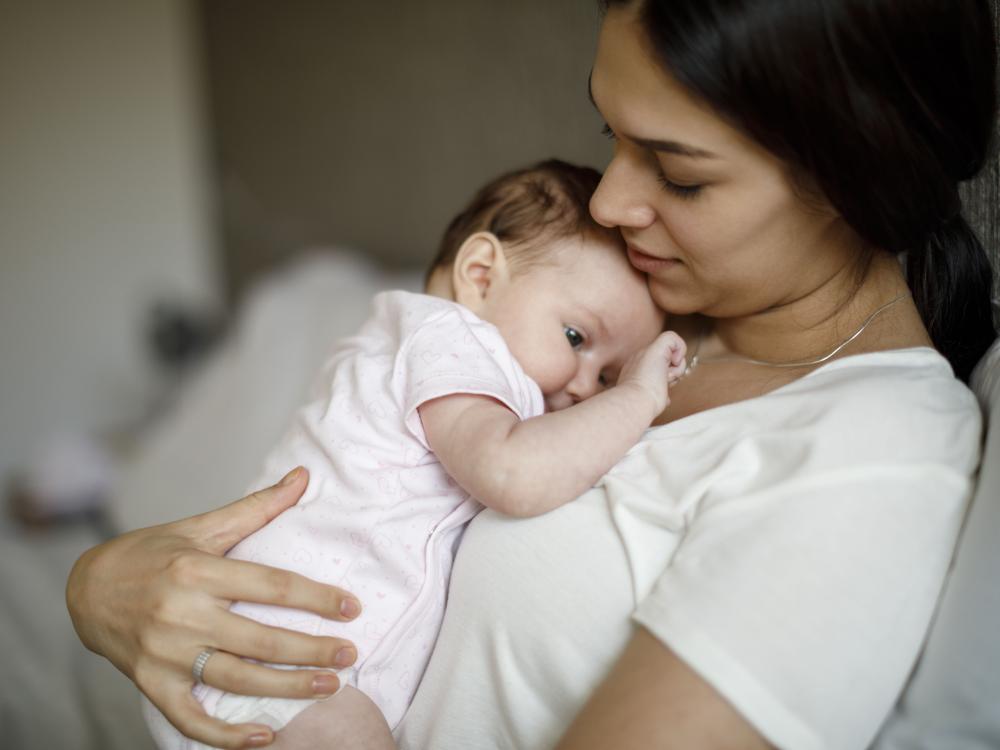 Young woman holds tired-looking baby as the baby touches her necklace