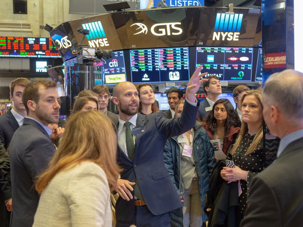 students watch man pointing at NYSE floor