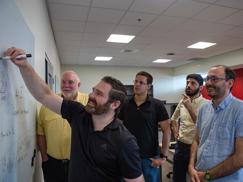 Five researchers gaze at a whiteboard in a classroom. 