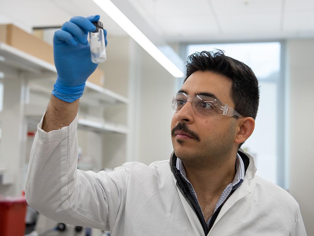 A individual wearing a lab coat stares at a small vial.