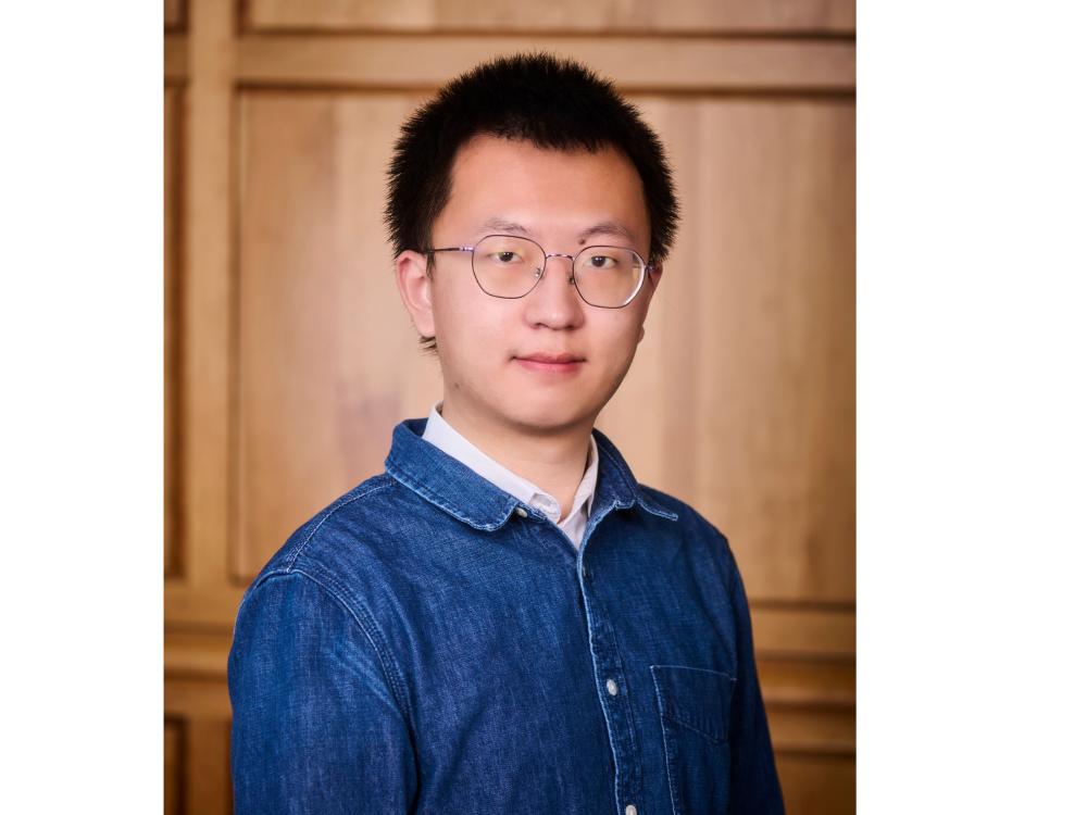 Yancheng Wang in front of wood paneling