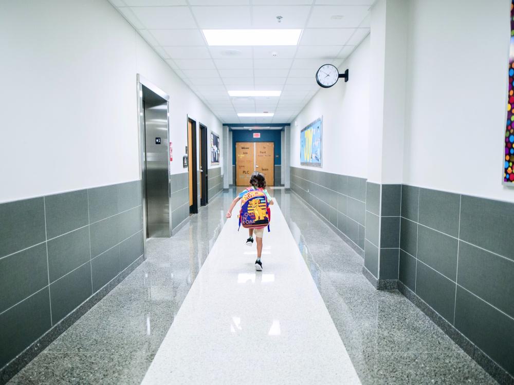 Child with backpack walking down a hallway at a school.