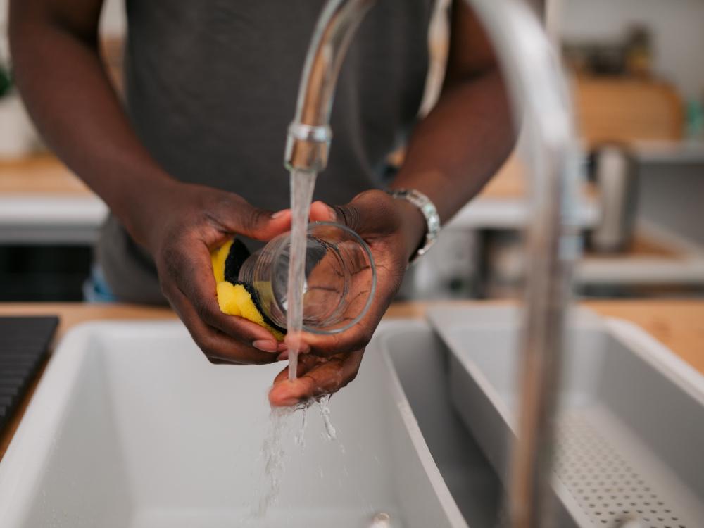 Man washing dishes using tap water in his kitchen