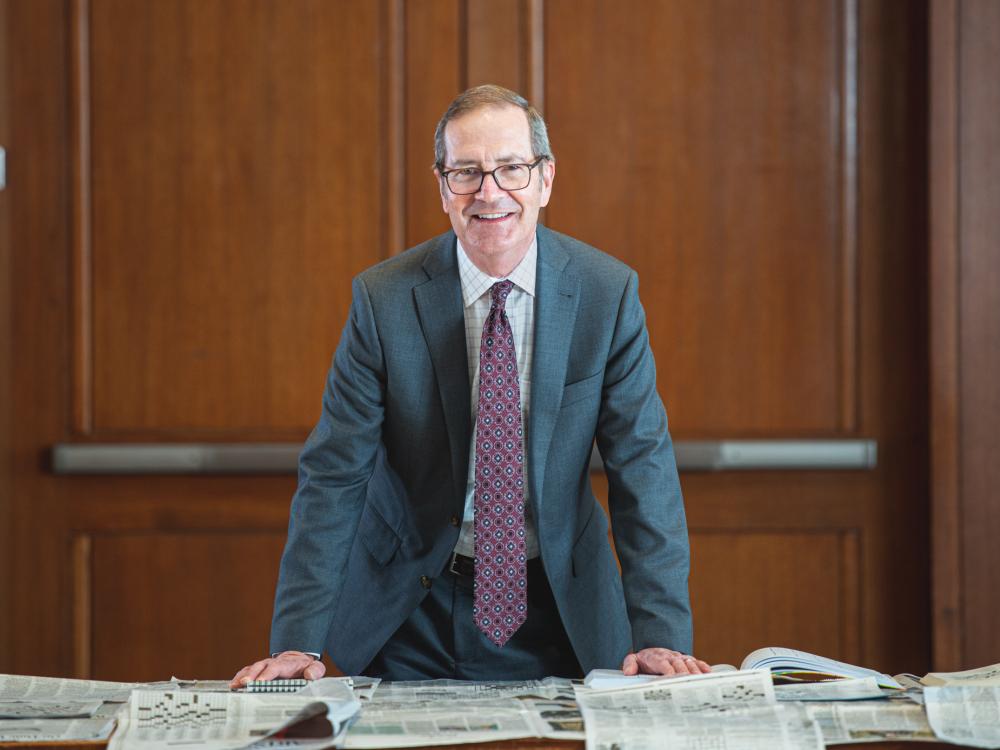Charles Whiteman, John and Karen Arnold Dean of the Smeal College of Business, leans over a desk covered in newspapers. Wood-paneled doors are behind him.