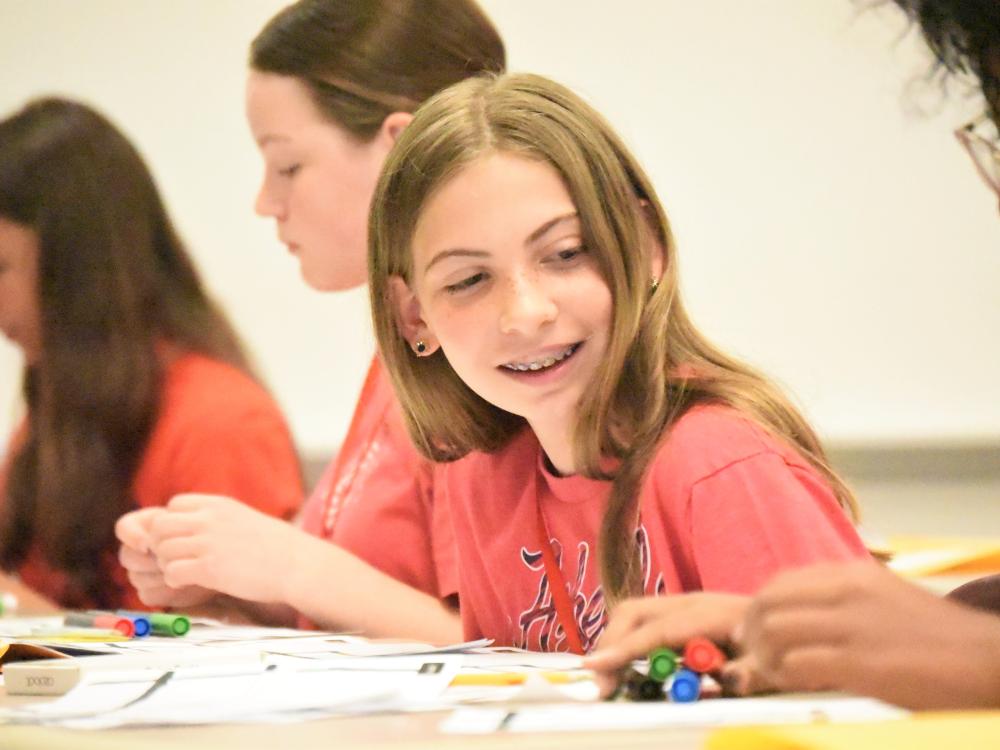 A middle-schooler looks to her side and smiles as a classmate works on a drawing project.