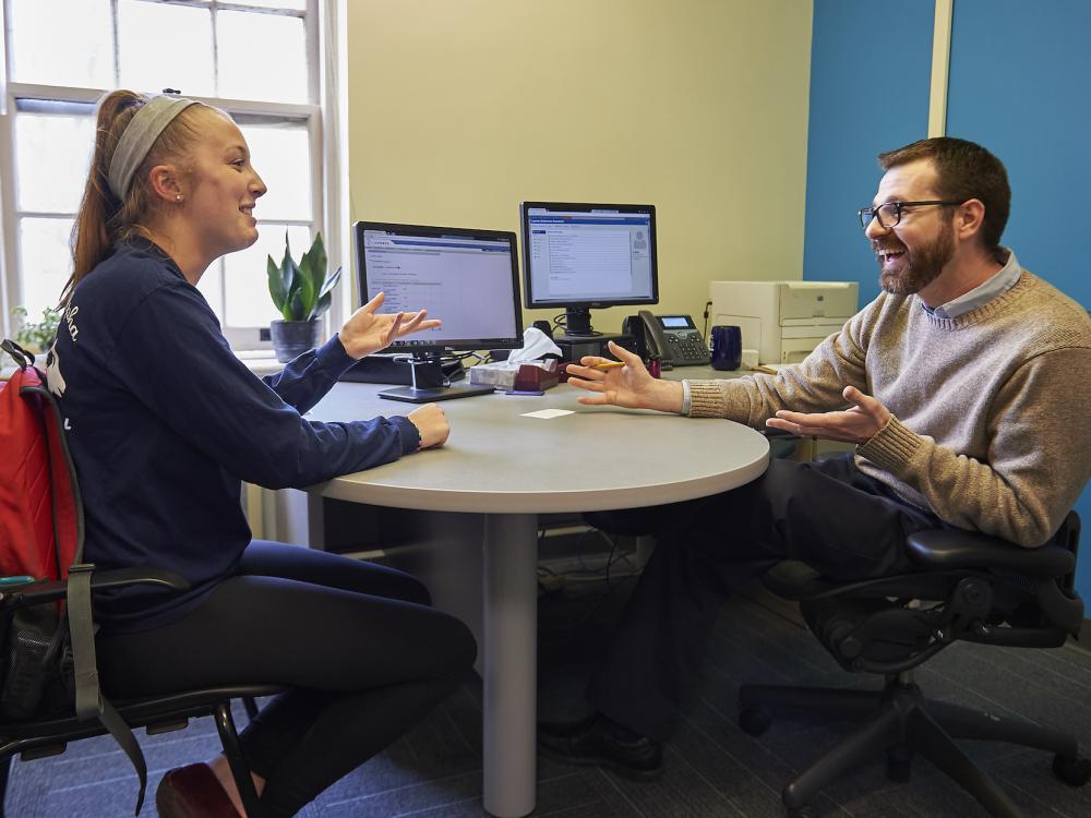 Student sitting across from academic adviser talking and smiling