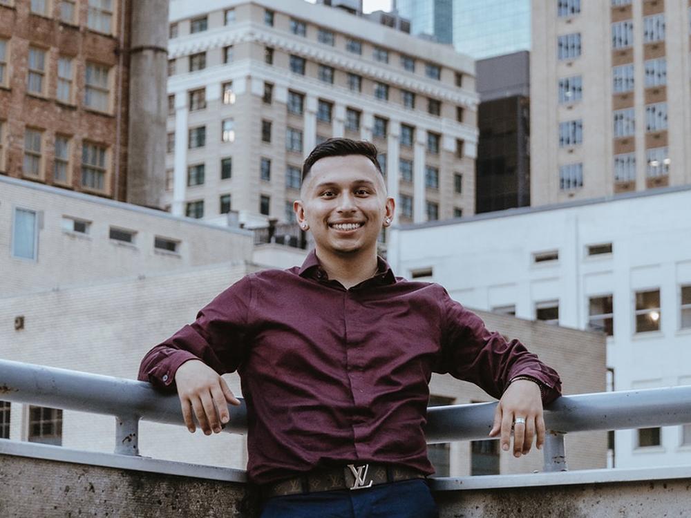 Liberal Arts student Michael Garza poses on a rooftop and smiles at the camera