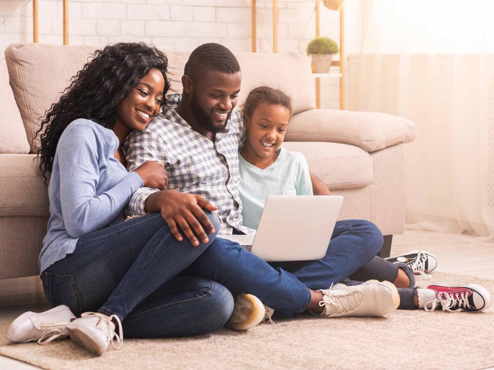 smiling parents and daugher looking at a laptop computer together