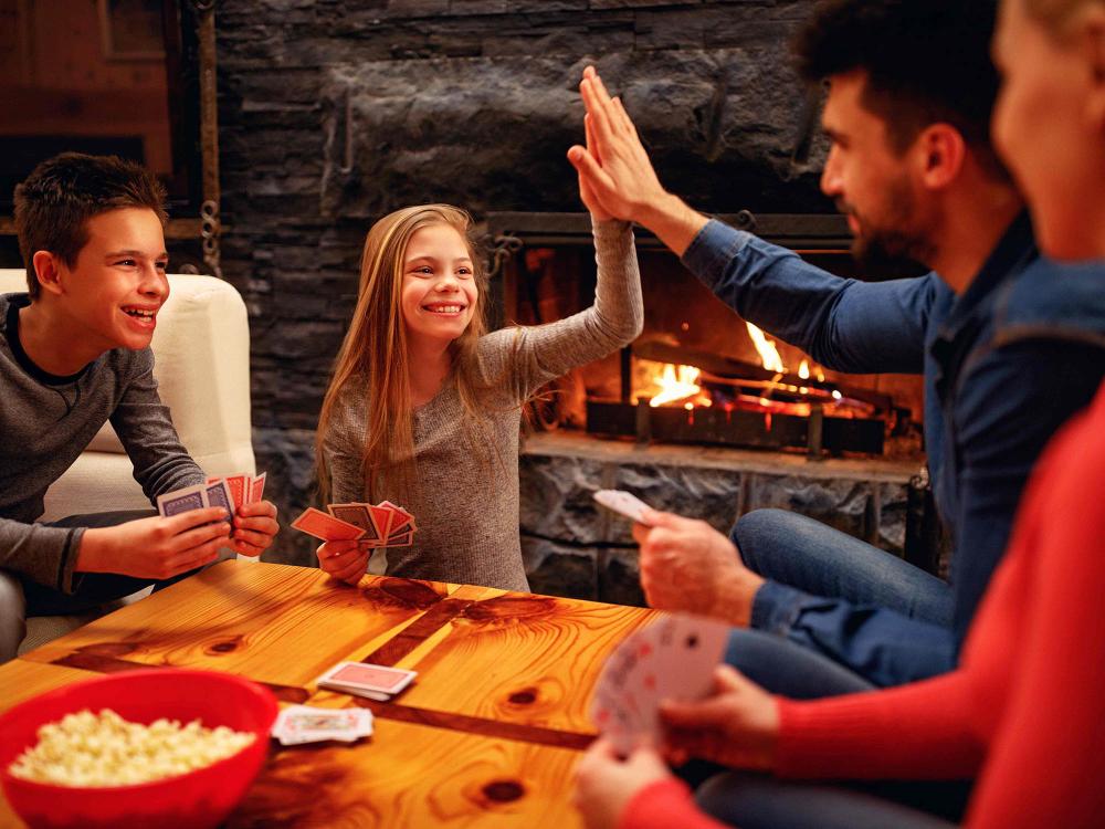 family of four playing cards in front of the fireplace, daughter gives father a high-five