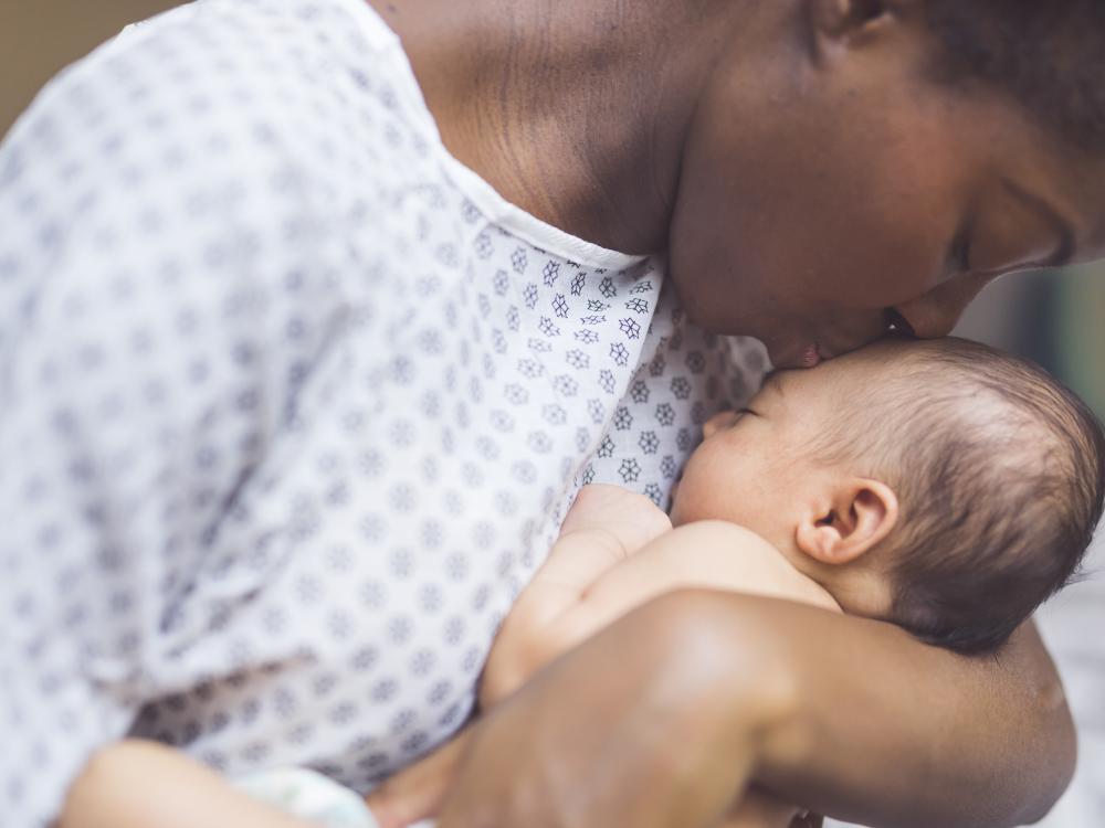 Mother wearing hospital gown kisses newborn gently on the head