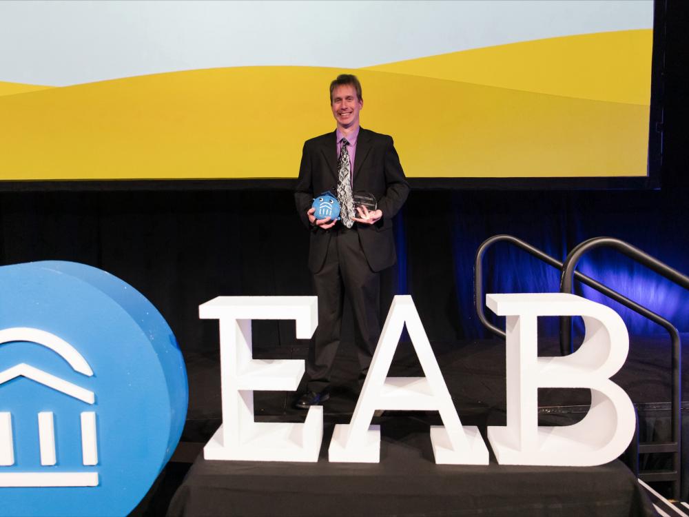 John Ellenberger posing on stage holding awards