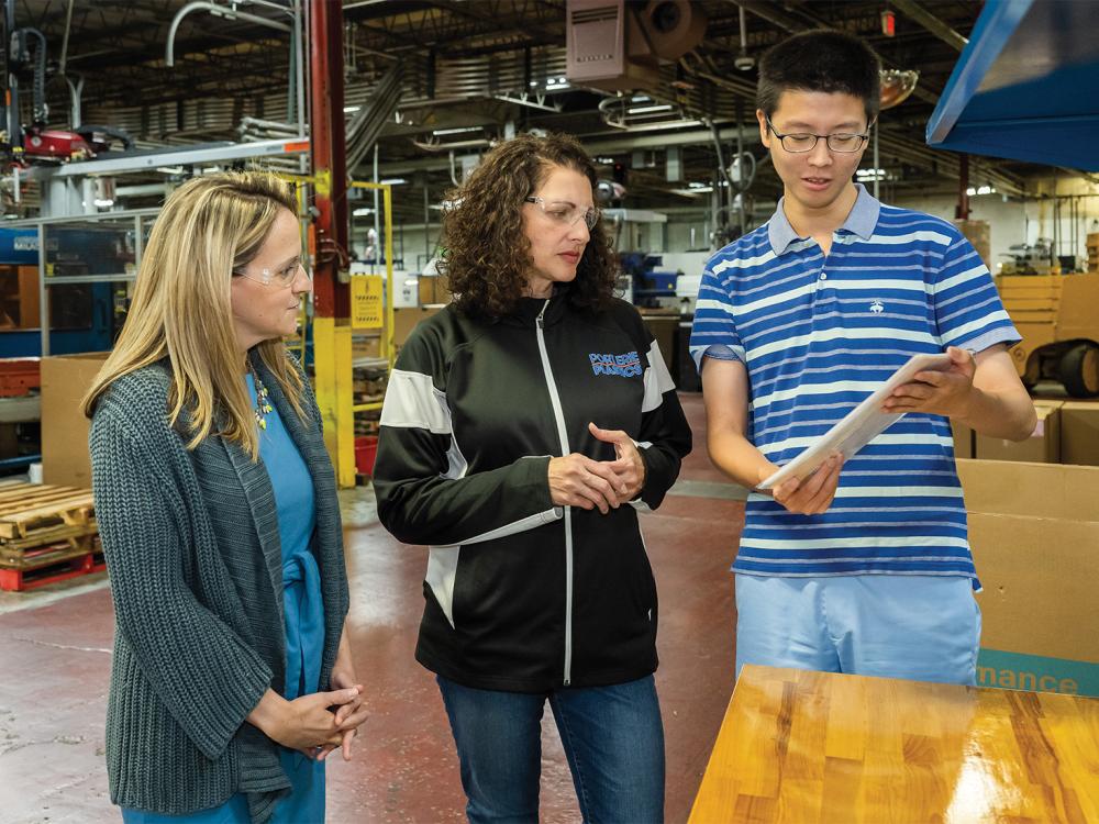 A Penn State Behrend student shows a sign he translated to a professor and a corporate executive during a visit to the shop floor at Port Erie Plastics.