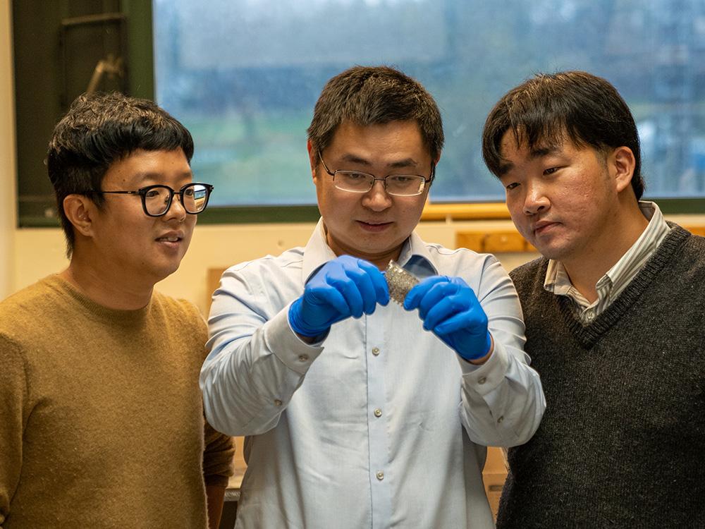 Three people examine a small square device.