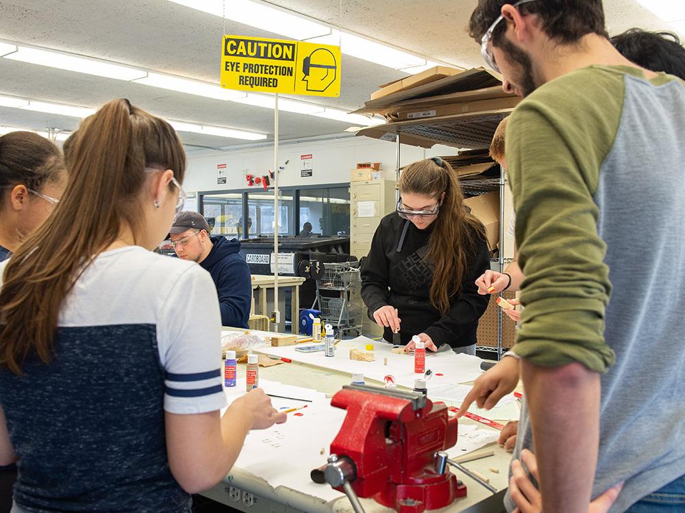 Students stand around a work bench, working with glue and schematics.