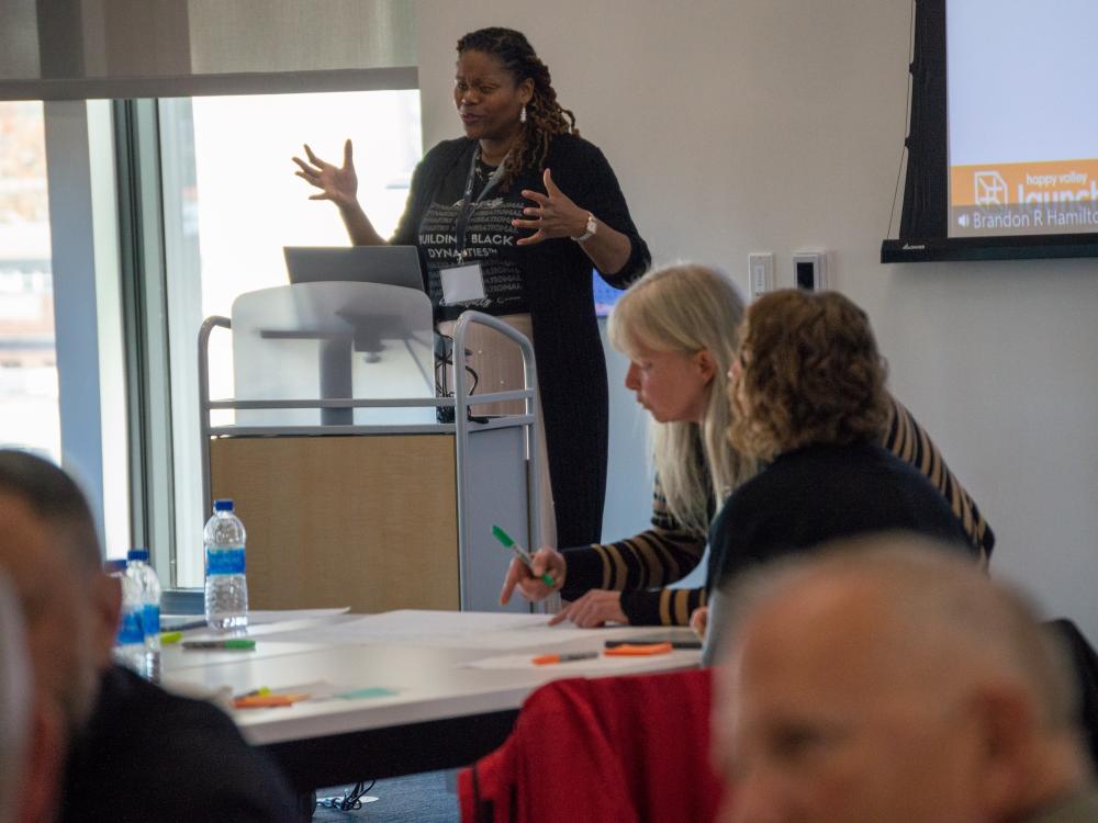 Woman at podium leads exercise with conference attendees at table