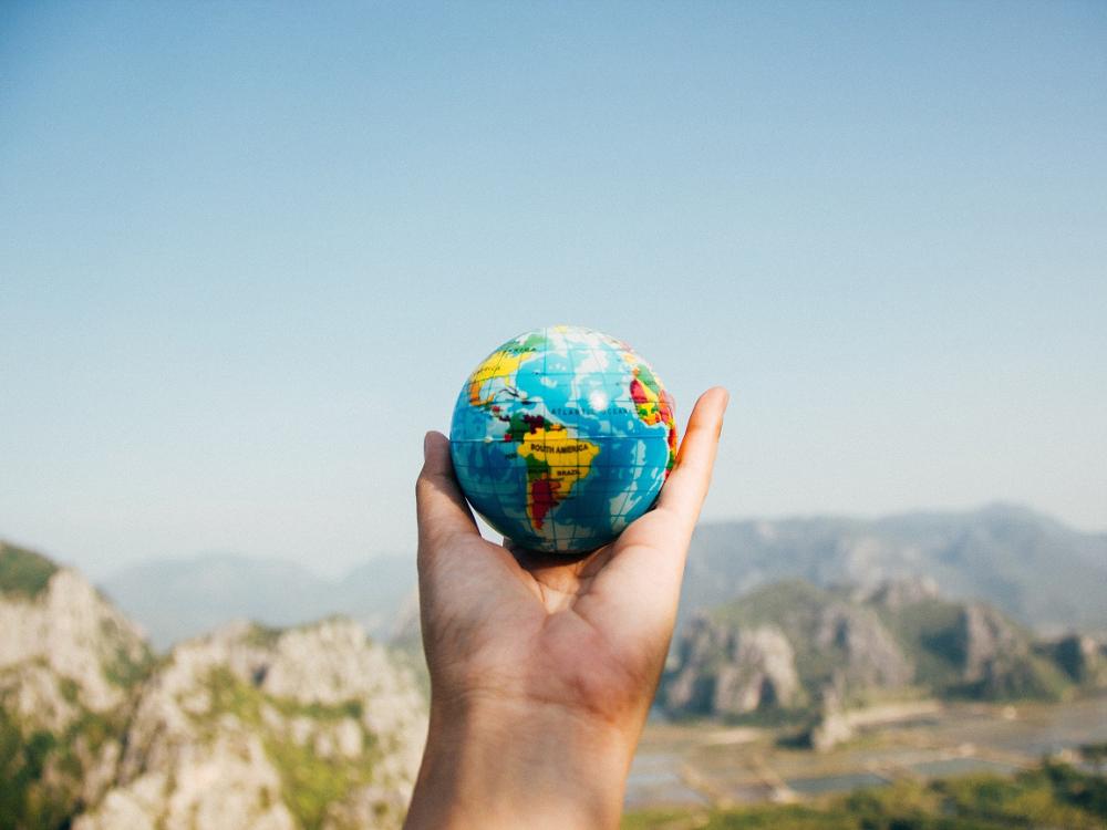 A hand holding a globe with mountains in the background