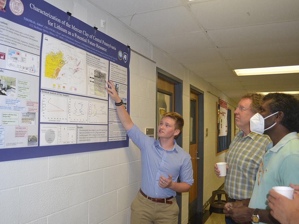 Aiden Thomas points to a poster on a wall as three people look on