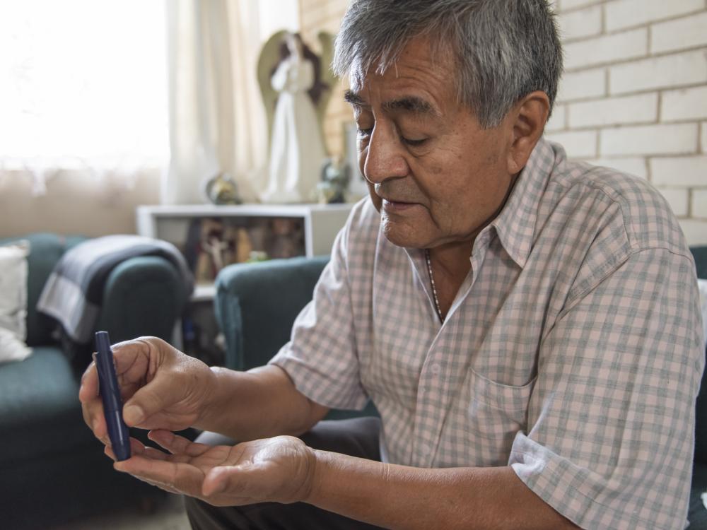 Older Hispanic man sticks his finger to test his blood sugar