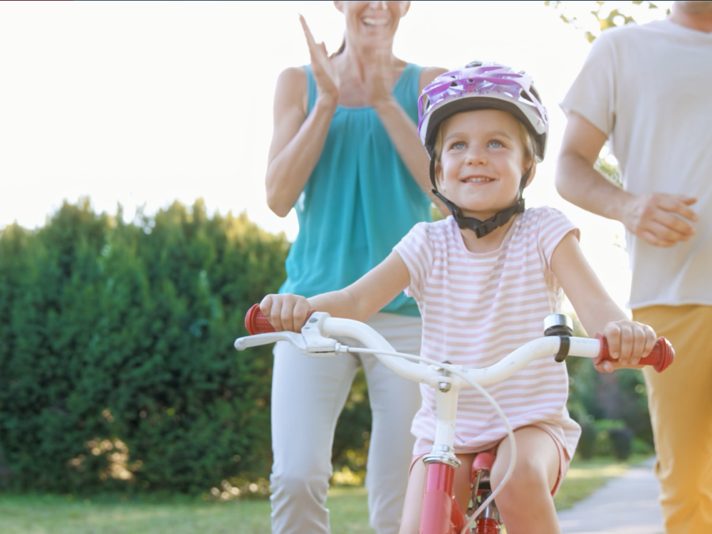 Happy child rides bike while parents watch in the background