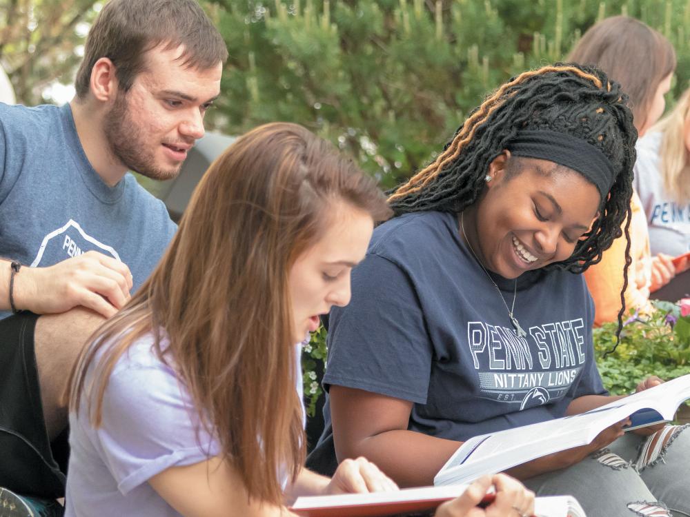 Three students sitting outside looking at textbooks