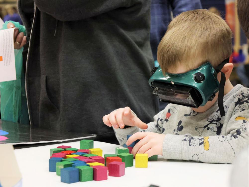 A boy stacks blocks while wearing VR goggles at the Penn State Behrend STEAM fair.