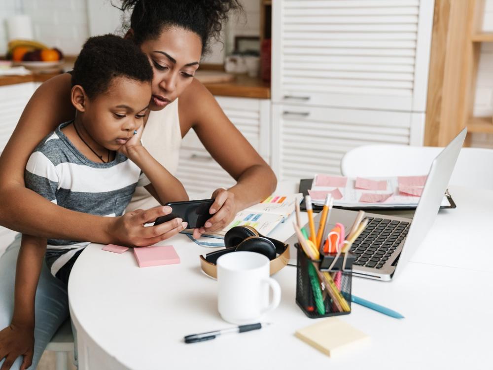 Black mother and son using mobile phone while sitting together at home