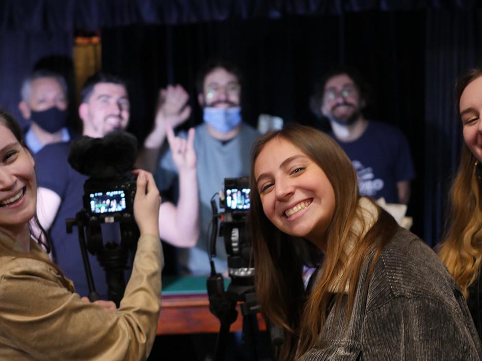 Three smiling students in the foreground with the subject of their focus behind them