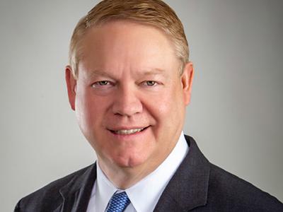 A headshot of Scott Cunningham wearing a dark suit, white shirt and blue tie.