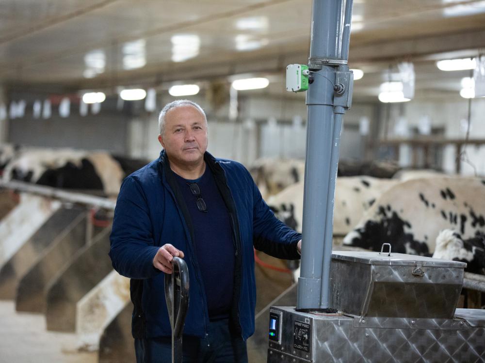 A man stands in a facilty with rows of cows behind him in stalls