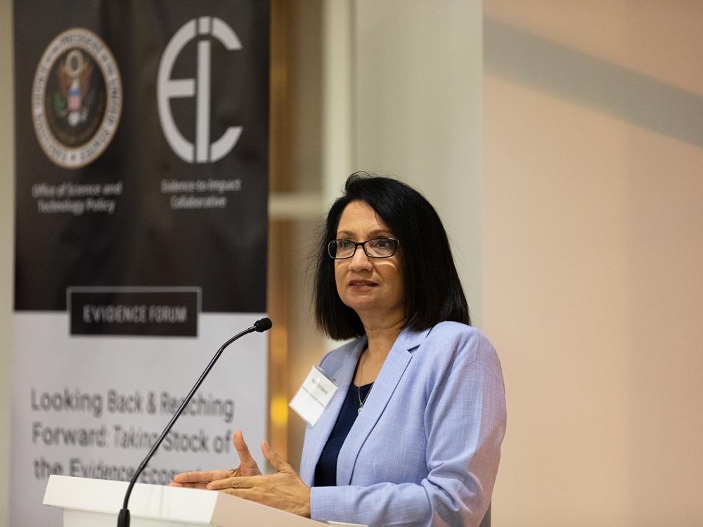 Penn State President Neeli Bendapudi speaks at a podium in front of a banner displaying the White House Office of Science and Technology Policy and Penn State's Evidence-to-Impact Collaborative