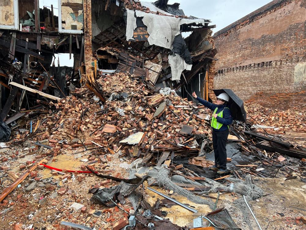 An individual looks toward and points at a large pile of building materials, bricks and rubble.