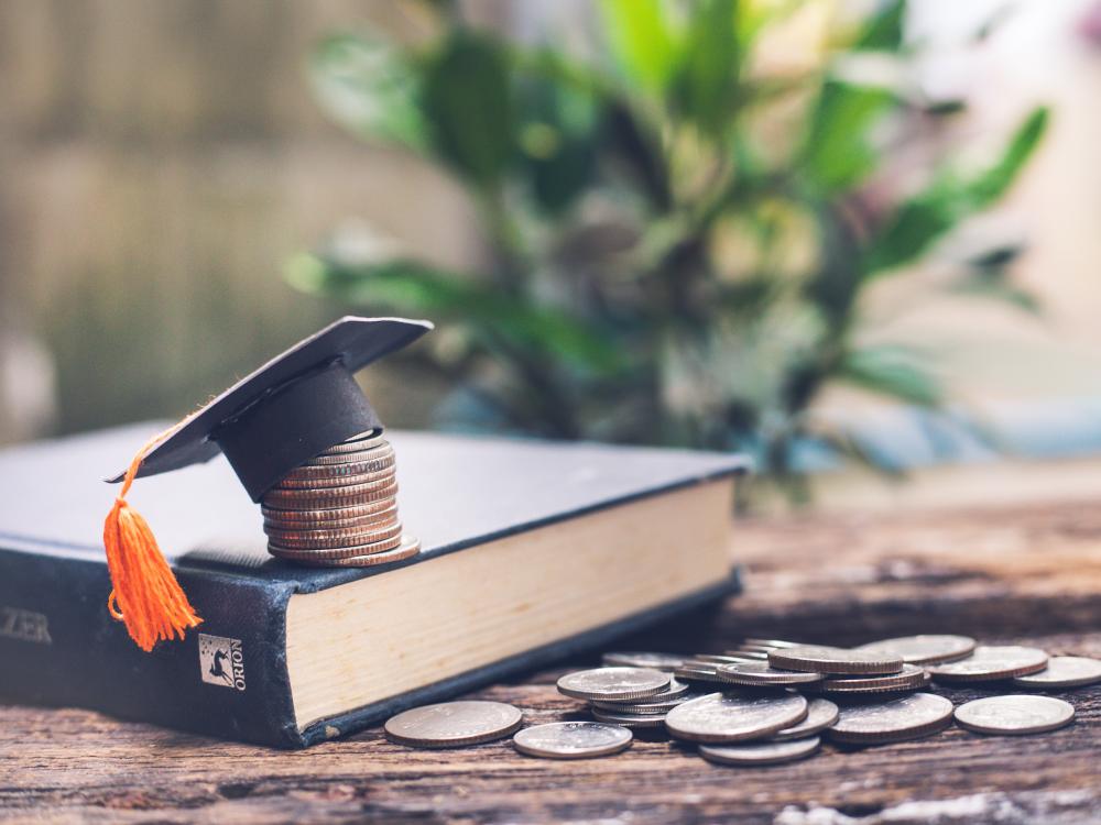 coin pile near book, coin stack on book cover and paper graduation cap atop stack