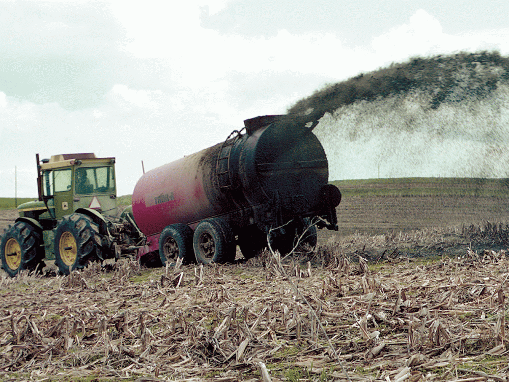 A tractor fertilizing a field with manure in a big, long spray