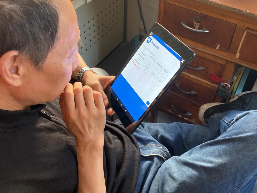 A man sits at a desk holding a tablet that has a Penn State-branded survey on the screen. 