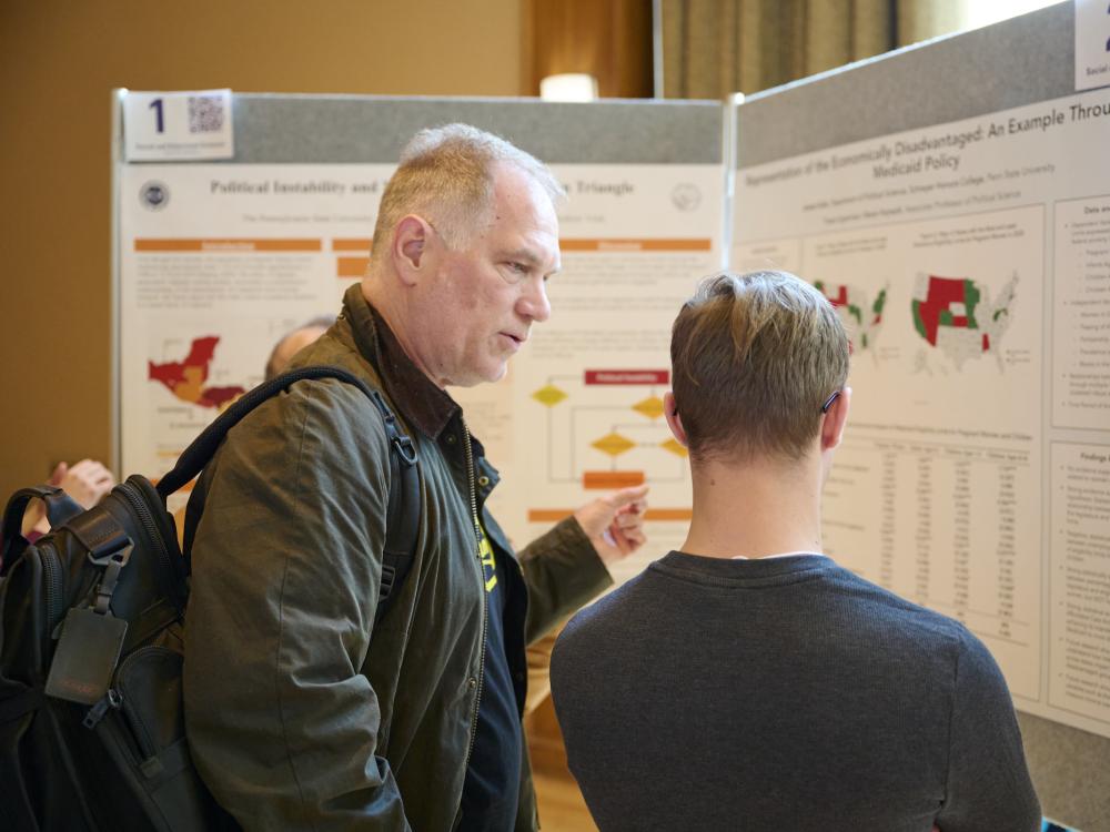 Faculty judge talking with student in front of research poster