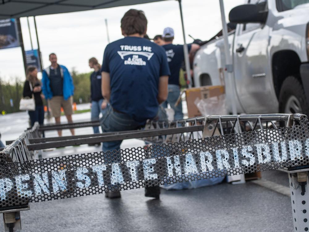 A student sits on the edge of a steel bridge that has "Penn State Harrisburg" painted on it