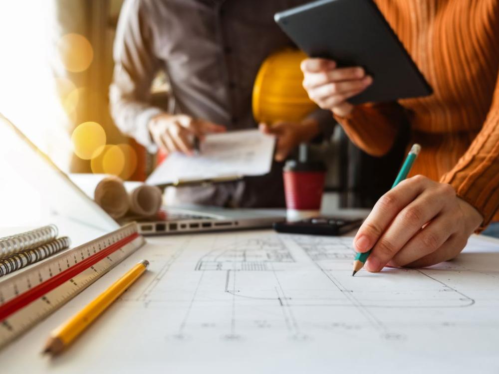 Two colleagues discussing data working and tablet, laptop with on on architectural project at construction site at desk in office