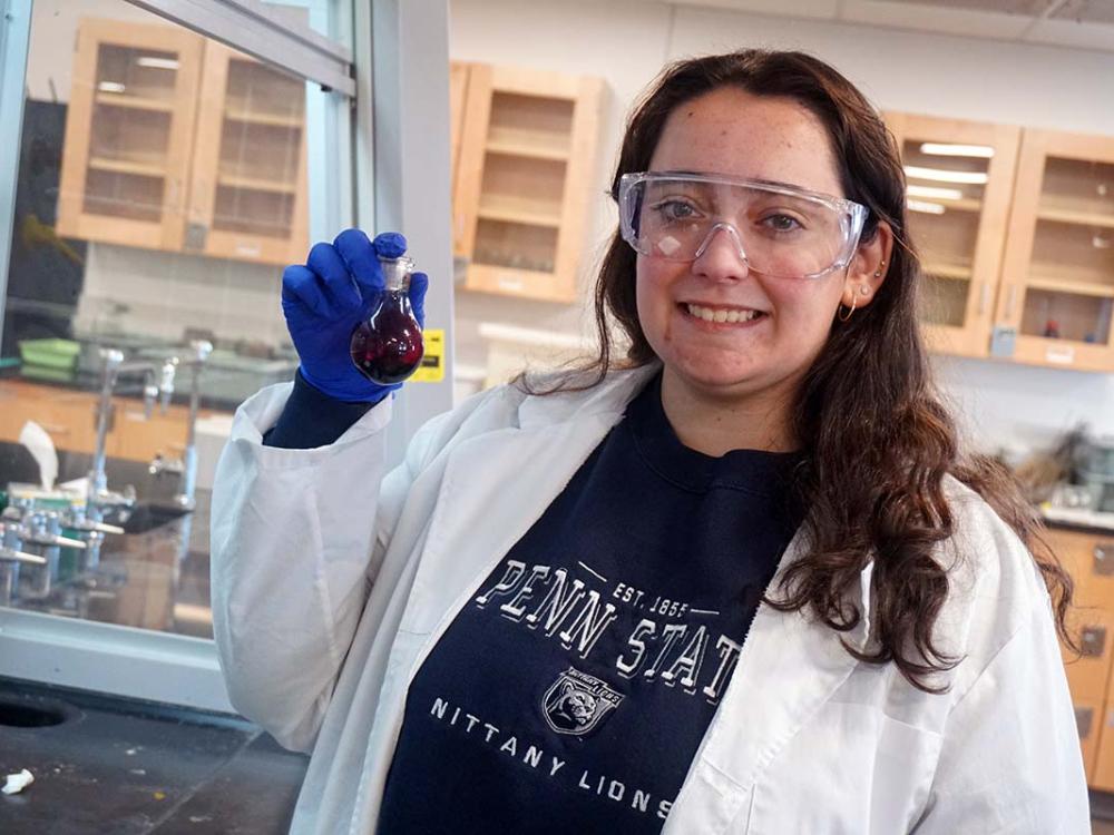 Woman in lab coat holding beaker of purple liquid in a science laboratory.