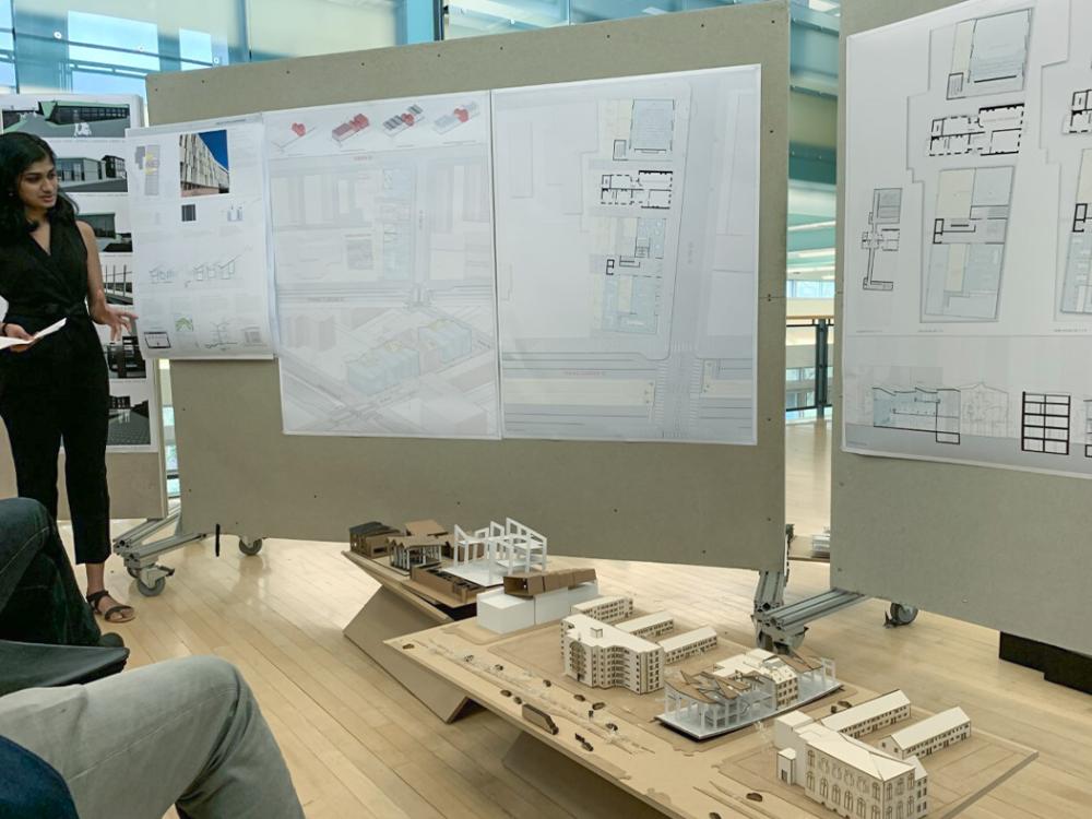 Anjali Gopalakrishnan at left with an architectural model she built before her and her architectural drawings pinned up on boards behind her.
