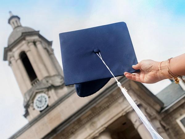 Graduate holding blue graduation cap in front of Old Main