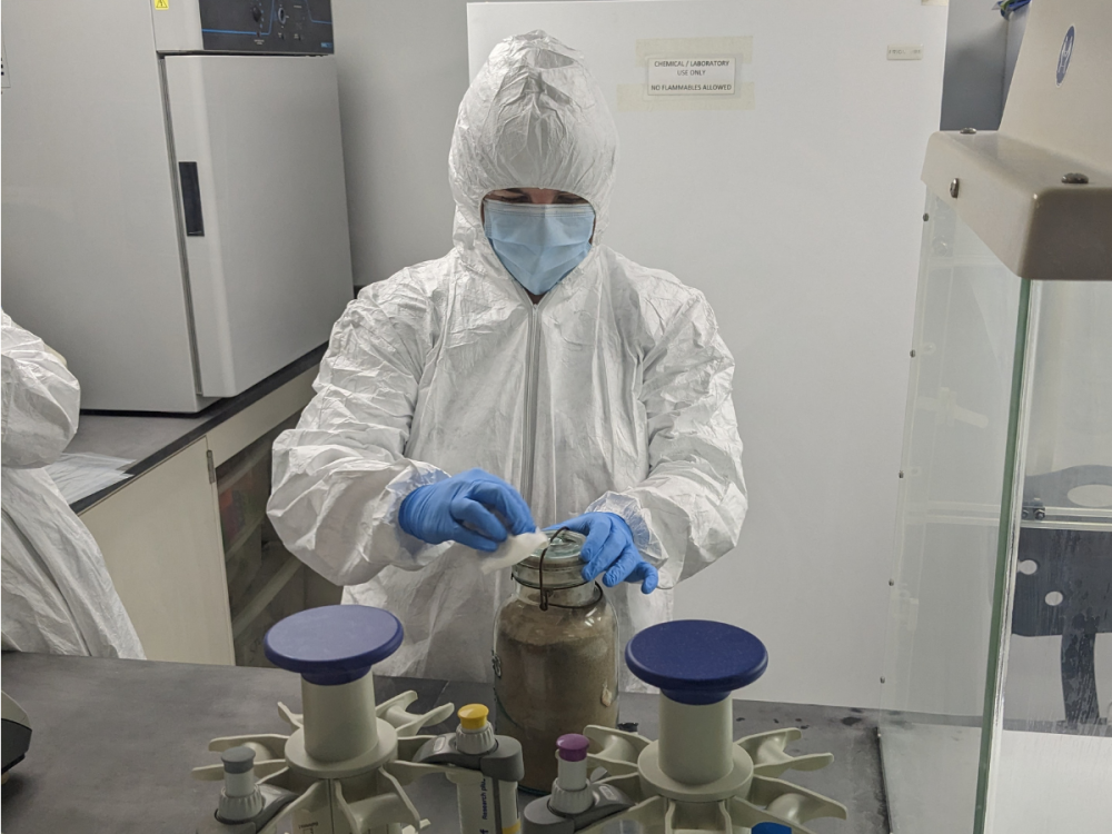 A researcher in full PPE prepares a jar of soil to be opened