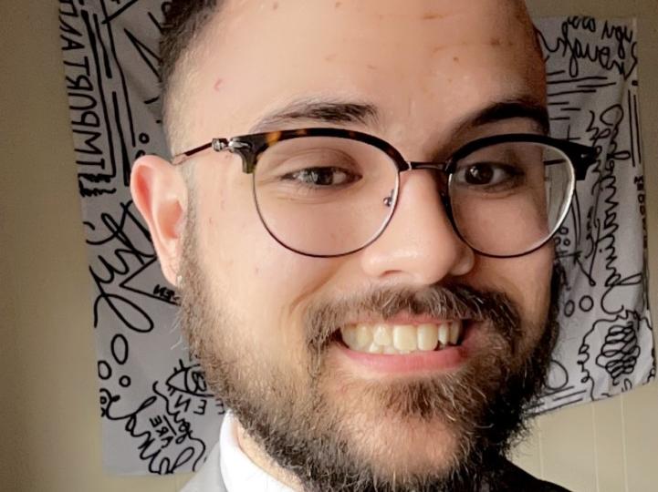 Head shot of a young man with dark hair and dark-rimmed glasses smiling