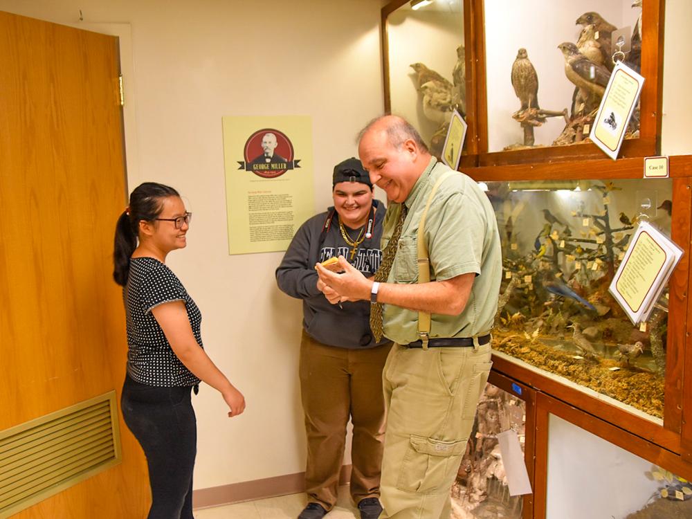 Two female students with a male faculty member examing a specimen at a museum