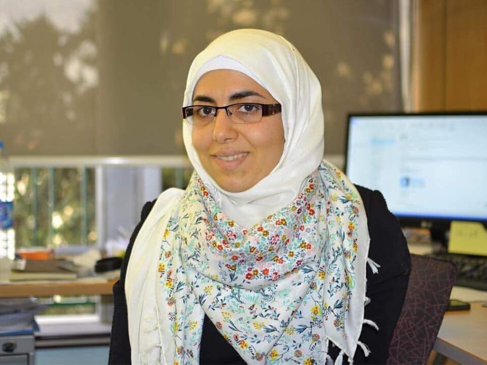 A photo of Dima Abu-Aridah in a headscarf, sitting in front of a computer.