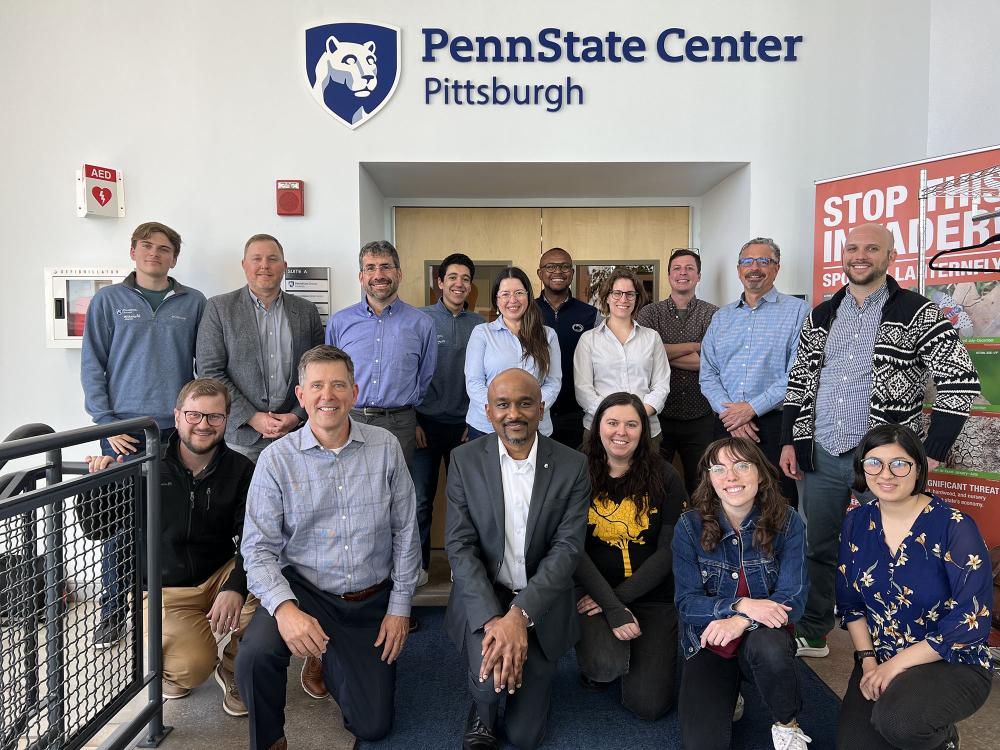 A group of people stand outside a doorway with the words "Penn State Center Pittsburgh" on the wall behind them. 