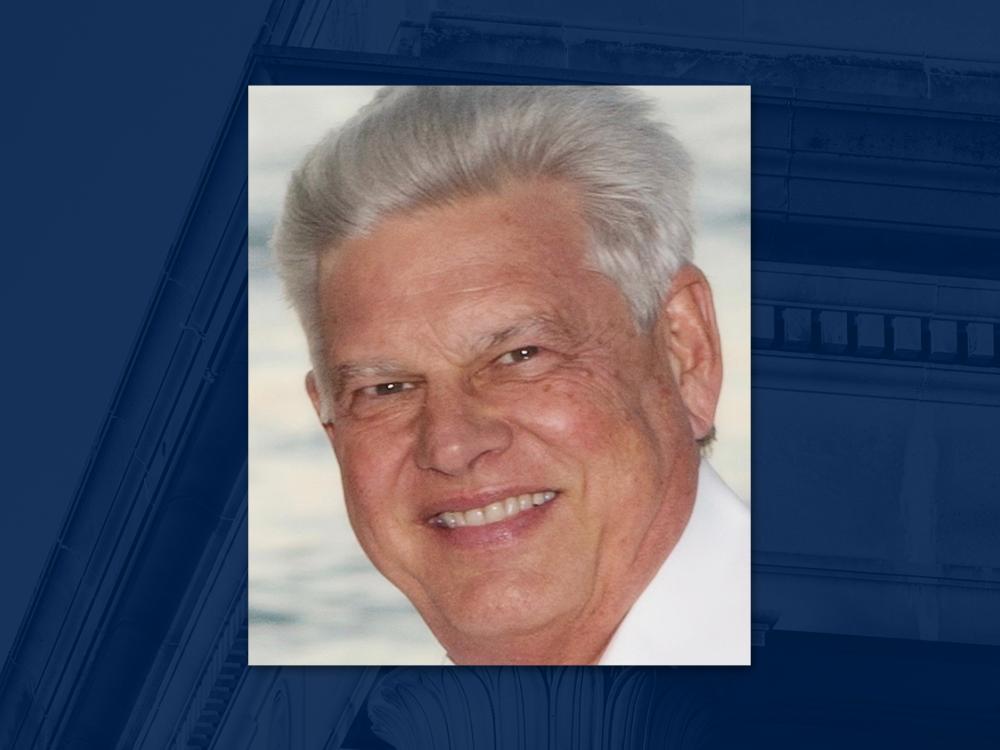 Headshot of smiling person wearing white collared shirt. Ocean can be seen in background.