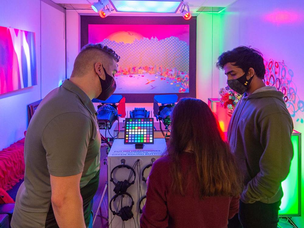 Three individuals look at a lighting board in a colorfully-lit room.